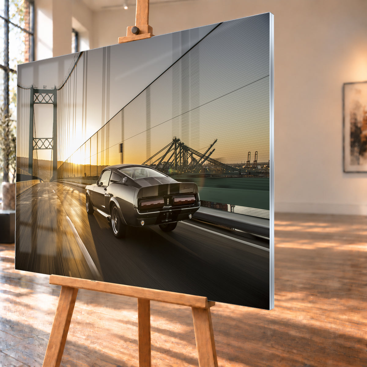 Dunkelgrauer Ford Mustang Fastback in Heck-Dreiviertelansicht auf einer Hängebrücke; goldenes Gegenlicht spiegelt sich auf der Fahrbahn, rechts sind Wasser und Hafenkräne zu sehen; Visualisierung als Acrylglas-Wandbild, schräg von der Seite auf einer Holzstaffelei.