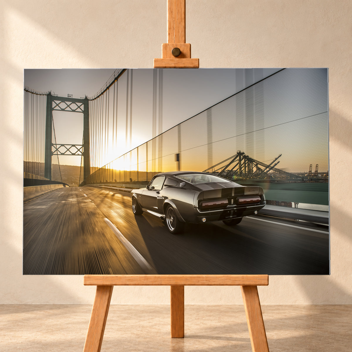 Dunkelgrauer Ford Mustang Fastback in Heck-Dreiviertelansicht auf einer Hängebrücke; goldenes Gegenlicht spiegelt sich auf der Fahrbahn, rechts sind Wasser und Hafenkräne zu sehen; Visualisierung als Alu gebürstet-Wandbild, frontal auf einer Holzstaffelei.