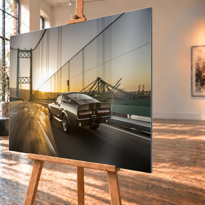 Dunkelgrauer Ford Mustang Fastback in Heck-Dreiviertelansicht auf einer Hängebrücke; goldenes Gegenlicht spiegelt sich auf der Fahrbahn, rechts sind Wasser und Hafenkräne zu sehen; Visualisierung als Alu gebürstet-Wandbild, schräg von der Seite auf einer Holzstaffelei.