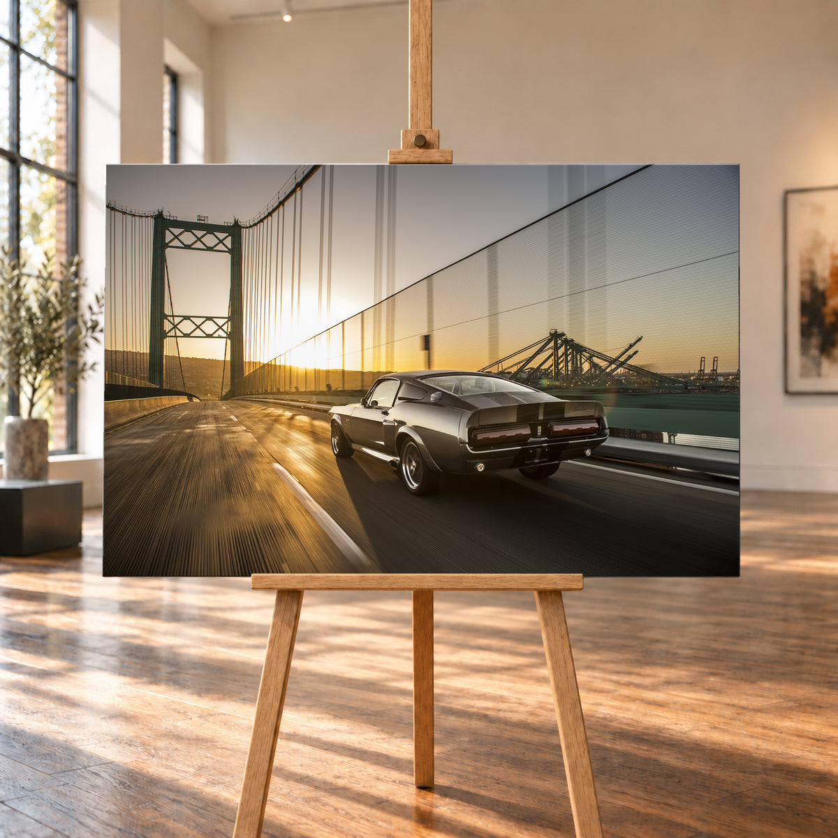 Dunkelgrauer Ford Mustang Fastback in Heck-Dreiviertelansicht auf einer Hängebrücke; goldenes Gegenlicht spiegelt sich auf der Fahrbahn, rechts sind Wasser und Hafenkräne zu sehen; Visualisierung als Leinwand-Wandbild, auf einer Holzstaffelei in einem hellen Galerieraum.