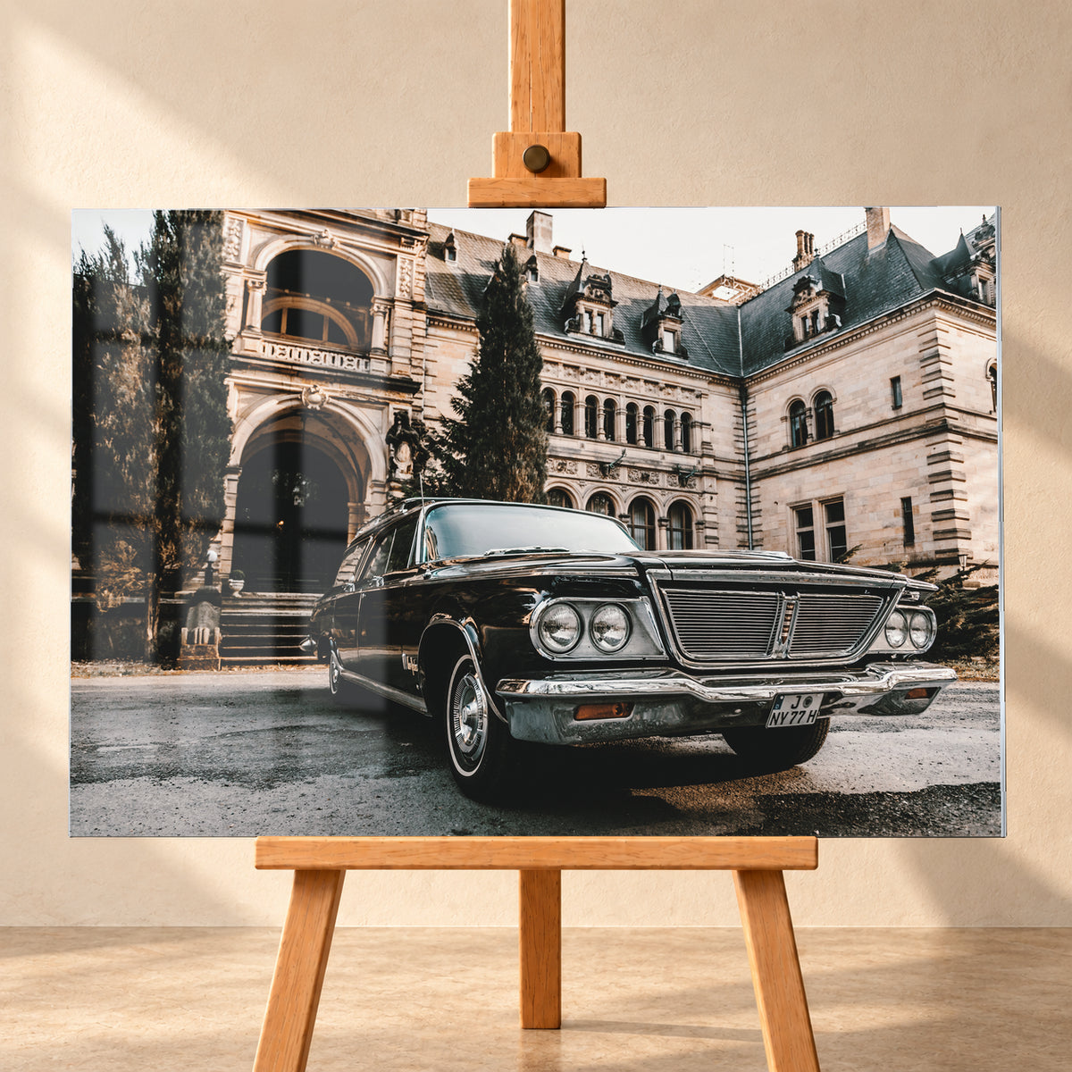 Dunkler Chrysler New Yorker Town & Country in niedriger Front-Dreiviertelansicht vor einem großen historischen Steingebäude mit Rundbögen; warmes Tageslicht spiegelt sich in Chromfront und Lack; Visualisierung als Acrylglas-Wandbild, frontal auf einer Holzstaffelei.
