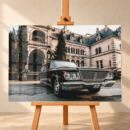 Dunkler Chrysler New Yorker Town & Country in niedriger Front-Dreiviertelansicht vor einem großen historischen Steingebäude mit Rundbögen; warmes Tageslicht spiegelt sich in Chromfront und Lack; Visualisierung als Acrylglas-Wandbild, frontal auf einer Holzstaffelei.