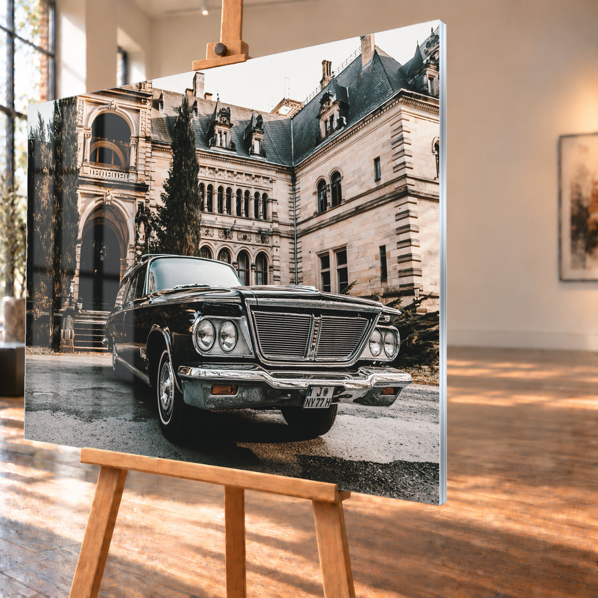 Dunkler Chrysler New Yorker Town & Country in niedriger Front-Dreiviertelansicht vor einem großen historischen Steingebäude mit Rundbögen; warmes Tageslicht spiegelt sich in Chromfront und Lack; Visualisierung als Acrylglas-Wandbild, schräg von der Seite auf einer Holzstaffelei.