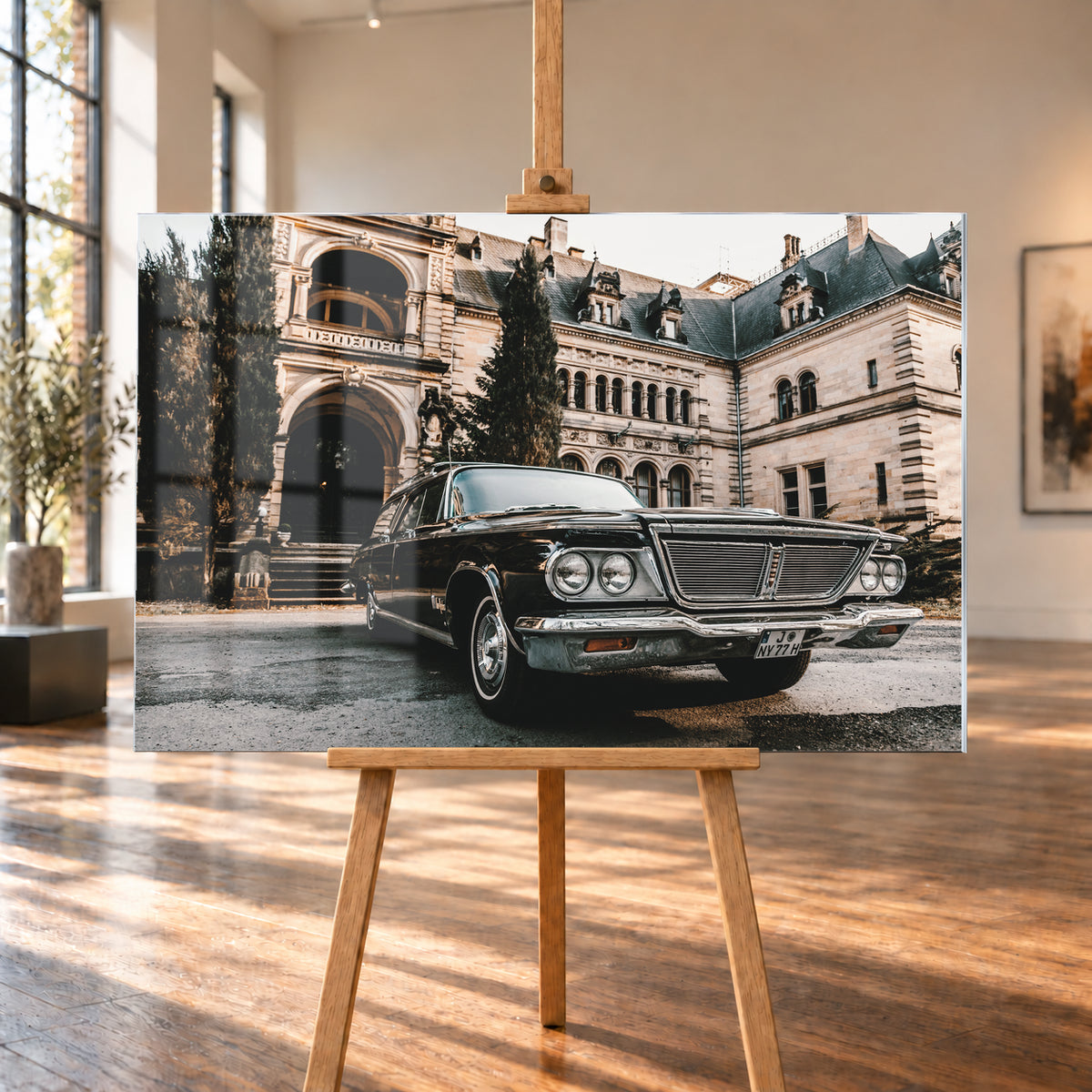 Dunkler Chrysler New Yorker Town & Country in niedriger Front-Dreiviertelansicht vor einem großen historischen Steingebäude mit Rundbögen; warmes Tageslicht spiegelt sich in Chromfront und Lack; Visualisierung als Acrylglas-Wandbild, auf einer Holzstaffelei in einem hellen Galerieraum.