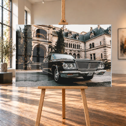 Dunkler Chrysler New Yorker Town & Country in niedriger Front-Dreiviertelansicht vor einem großen historischen Steingebäude mit Rundbögen; warmes Tageslicht spiegelt sich in Chromfront und Lack; Visualisierung als Acrylglas-Wandbild, auf einer Holzstaffelei in einem hellen Galerieraum.