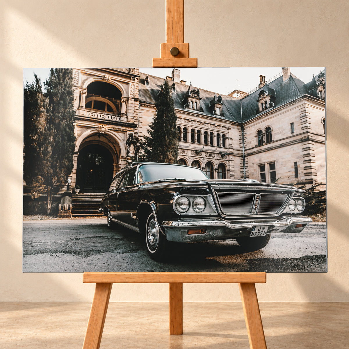 Dunkler Chrysler New Yorker Town & Country in niedriger Front-Dreiviertelansicht vor einem großen historischen Steingebäude mit Rundbögen; warmes Tageslicht spiegelt sich in Chromfront und Lack; Visualisierung als Alu gebürstet-Wandbild, frontal auf einer Holzstaffelei.
