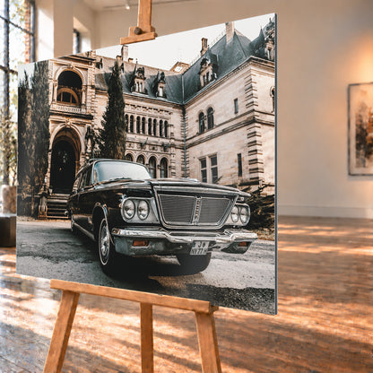 Dunkler Chrysler New Yorker Town & Country in niedriger Front-Dreiviertelansicht vor einem großen historischen Steingebäude mit Rundbögen; warmes Tageslicht spiegelt sich in Chromfront und Lack; Visualisierung als Alu gebürstet-Wandbild, schräg von der Seite auf einer Holzstaffelei.