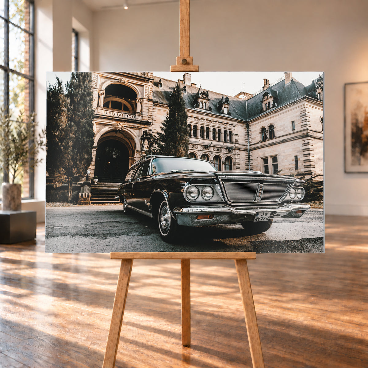 Dunkler Chrysler New Yorker Town & Country in niedriger Front-Dreiviertelansicht vor einem großen historischen Steingebäude mit Rundbögen; warmes Tageslicht spiegelt sich in Chromfront und Lack; Visualisierung als Alu gebürstet-Wandbild, auf einer Holzstaffelei in einem hellen Galerieraum.
