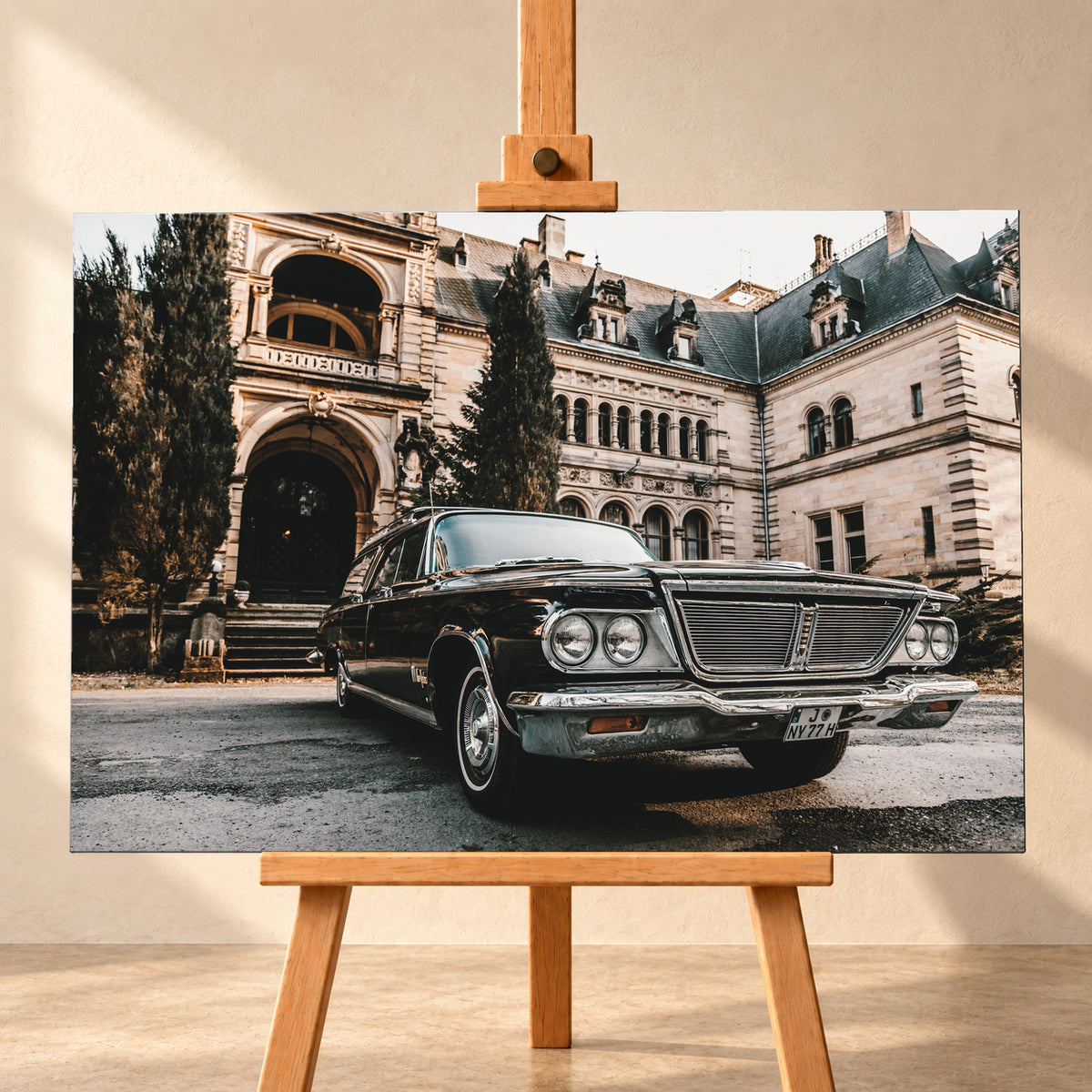 Dunkler Chrysler New Yorker Town & Country in niedriger Front-Dreiviertelansicht vor einem großen historischen Steingebäude mit Rundbögen; warmes Tageslicht spiegelt sich in Chromfront und Lack; Visualisierung als Leinwand-Wandbild, frontal auf einer Holzstaffelei.