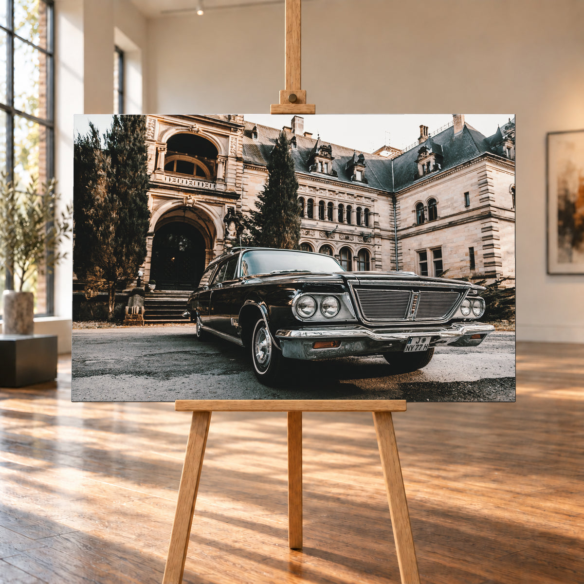 Dunkler Chrysler New Yorker Town & Country in niedriger Front-Dreiviertelansicht vor einem großen historischen Steingebäude mit Rundbögen; warmes Tageslicht spiegelt sich in Chromfront und Lack; Visualisierung als Leinwand-Wandbild, auf einer Holzstaffelei in einem hellen Galerieraum.