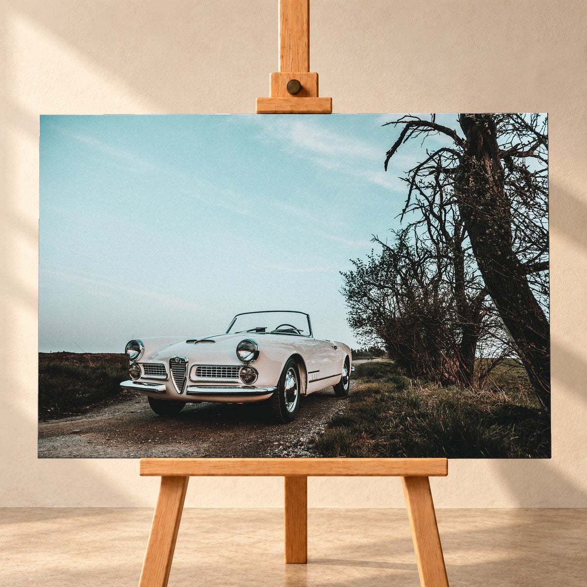 Heller Alfa Romeo 2000 Touring Spider in tiefer Front-Dreiviertelansicht auf einem schmalen Weg neben einem großen knorrigen Baum unter bläulichem, bewölktem Himmel; Visualisierung als Leinwand-Wandbild, frontal auf einer Holzstaffelei.