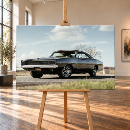 Dunkler Dodge Charger R/T in tiefer Dreiviertelansicht von vorn auf einer Straße unter hellem, wolkigem Himmel; im Hintergrund kahle Bäume und trockenes Gras; Visualisierung als Leinwand-Wandbild, auf einer Holzstaffelei in einem hellen Galerieraum.