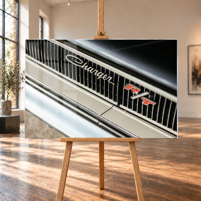 Diagonale Nahaufnahme eines hell lackierten Charger R/T mit schwarzem Lamellengrill, verchromtem Charger-Schriftzug und rot-weißem R/T-Emblem; Chromleisten reflektieren helles Licht; Visualisierung als Acrylglas-Wandbild, auf einer Holzstaffelei in einem hellen Galerieraum.
