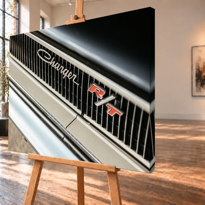 Diagonale Nahaufnahme eines hell lackierten Charger R/T mit schwarzem Lamellengrill, verchromtem Charger-Schriftzug und rot-weißem R/T-Emblem; Chromleisten reflektieren helles Licht; Visualisierung als Leinwand-Wandbild, schräg von der Seite auf einer Holzstaffelei.