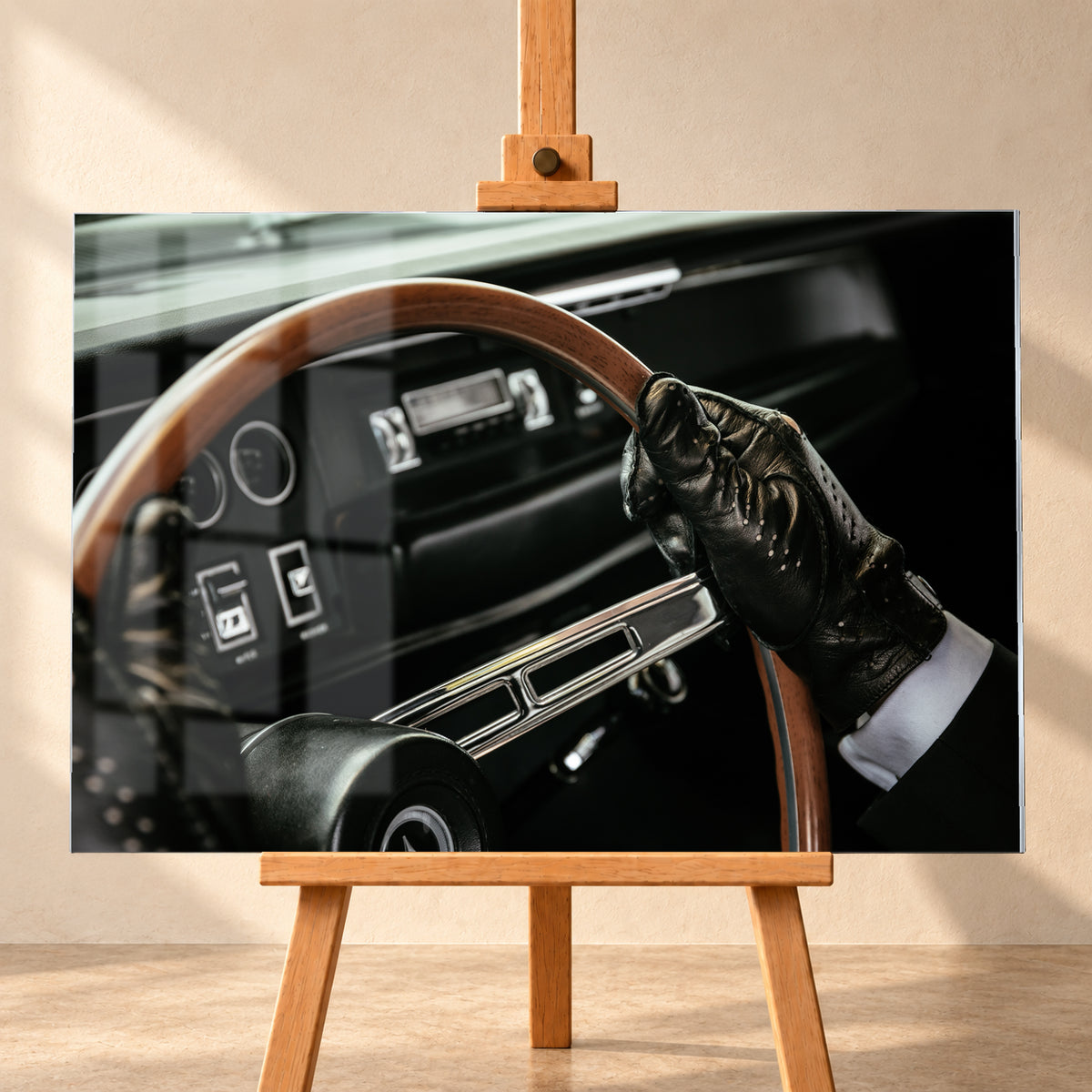 Nahaufnahme eines dunklen Fahrzeugcockpits: Eine Hand in schwarzem, perforiertem Handschuh greift ein braunes, holzfarbenes Lenkrad. Rundinstrumente, Radio und Armaturenbrett liegen unscharf im Hintergrund; seitliches Licht hebt Handschuh, Lenkradkranz und metallisch glänzende Speiche hervor; Visualisierung als Acrylglas-Wandbild, frontal auf einer Holzstaffelei.