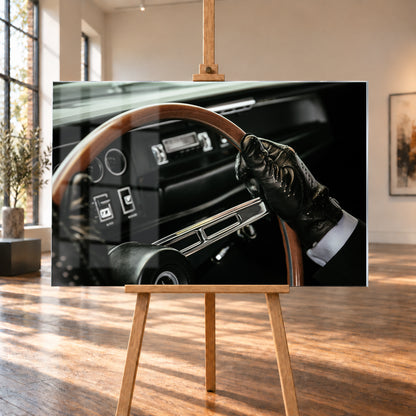 Nahaufnahme eines dunklen Fahrzeugcockpits: Eine Hand in schwarzem, perforiertem Handschuh greift ein braunes, holzfarbenes Lenkrad. Rundinstrumente, Radio und Armaturenbrett liegen unscharf im Hintergrund; seitliches Licht hebt Handschuh, Lenkradkranz und metallisch glänzende Speiche hervor; Visualisierung als Acrylglas-Wandbild, auf einer Holzstaffelei in einem hellen Galerieraum.