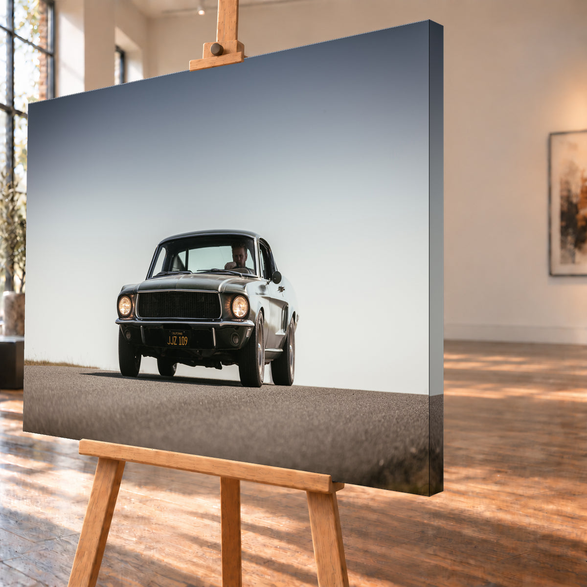 Dunkelgrüner klassischer Ford Mustang in tiefer Frontansicht auf Asphalt, mit eingeschalteten Rundscheinwerfern, sichtbarem Fahrer und weitem hellgrauem Himmel; Visualisierung als Leinwand-Wandbild, schräg von der Seite auf einer Holzstaffelei.