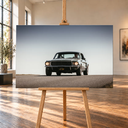 Dunkelgrüner klassischer Ford Mustang in tiefer Frontansicht auf Asphalt, mit eingeschalteten Rundscheinwerfern, sichtbarem Fahrer und weitem hellgrauem Himmel; Visualisierung als Leinwand-Wandbild, auf einer Holzstaffelei in einem hellen Galerieraum.