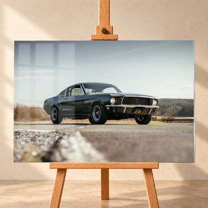 Dunkelgrüner Ford Mustang in niedriger Dreiviertelansicht von vorn auf Asphalt; dahinter offene Felder, ein bewaldeter Horizont und heller Himmel bei Tageslicht; Visualisierung als Acrylglas-Wandbild, frontal auf einer Holzstaffelei.