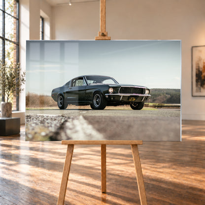Dunkelgrüner Ford Mustang in niedriger Dreiviertelansicht von vorn auf Asphalt; dahinter offene Felder, ein bewaldeter Horizont und heller Himmel bei Tageslicht; Visualisierung als Acrylglas-Wandbild, auf einer Holzstaffelei in einem hellen Galerieraum.