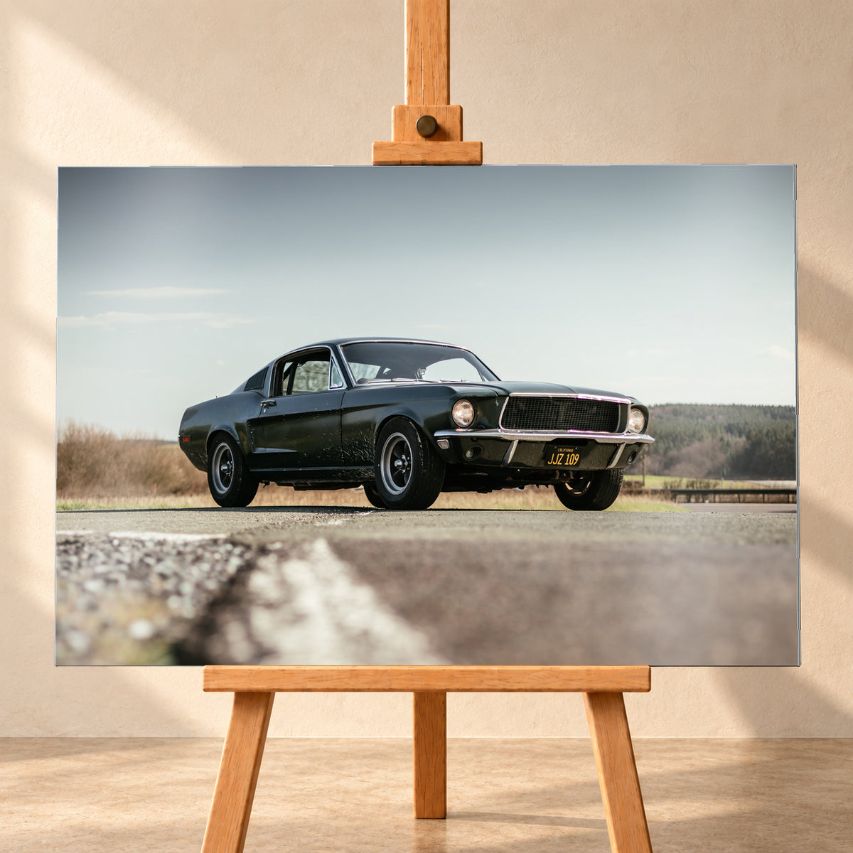 Dunkelgrüner Ford Mustang in niedriger Dreiviertelansicht von vorn auf Asphalt; dahinter offene Felder, ein bewaldeter Horizont und heller Himmel bei Tageslicht; Visualisierung als Alu gebürstet-Wandbild, frontal auf einer Holzstaffelei.