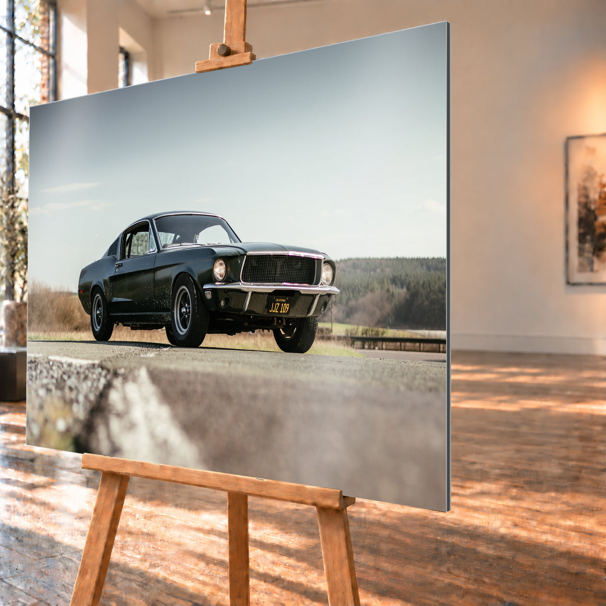 Dunkelgrüner Ford Mustang in niedriger Dreiviertelansicht von vorn auf Asphalt; dahinter offene Felder, ein bewaldeter Horizont und heller Himmel bei Tageslicht; Visualisierung als Alu gebürstet-Wandbild, schräg von der Seite auf einer Holzstaffelei.