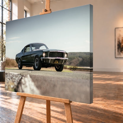 Dunkelgrüner Ford Mustang in niedriger Dreiviertelansicht von vorn auf Asphalt; dahinter offene Felder, ein bewaldeter Horizont und heller Himmel bei Tageslicht; Visualisierung als Leinwand-Wandbild, schräg von der Seite auf einer Holzstaffelei.