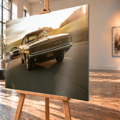 Dunkel erscheinender Dodge Charger R/T aus tiefer Frontperspektive auf einer kurvigen Landstraße; dahinter folgt ein weiteres dunkles Coupé. Goldenes Gegenlicht, grüne Hügel und starke Bewegungsunschärfe prägen die Fahrszene; Visualisierung als Alu gebürstet-Wandbild, schräg von der Seite auf einer Holzstaffelei.