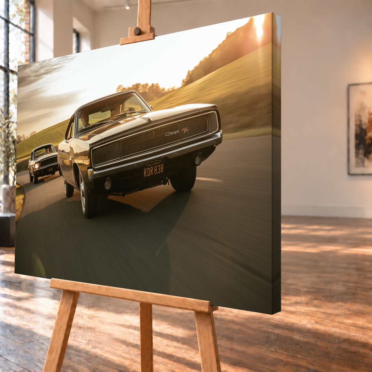 Dunkel erscheinender Dodge Charger R/T aus tiefer Frontperspektive auf einer kurvigen Landstraße; dahinter folgt ein weiteres dunkles Coupé. Goldenes Gegenlicht, grüne Hügel und starke Bewegungsunschärfe prägen die Fahrszene; Visualisierung als Leinwand-Wandbild, schräg von der Seite auf einer Holzstaffelei.