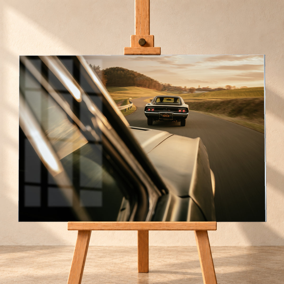 Dunkler Dodge Charger 440 R/T von hinten auf einer kurvigen Landstraße im goldenen Abendlicht, fotografiert aus einem zweiten fahrenden Auto; rote Rückleuchten, Wiesen und Bewegungsunschärfe; Visualisierung als Acrylglas-Wandbild, frontal auf einer Holzstaffelei.