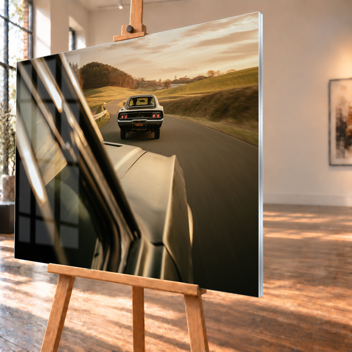 Dunkler Dodge Charger 440 R/T von hinten auf einer kurvigen Landstraße im goldenen Abendlicht, fotografiert aus einem zweiten fahrenden Auto; rote Rückleuchten, Wiesen und Bewegungsunschärfe; Visualisierung als Acrylglas-Wandbild, schräg von der Seite auf einer Holzstaffelei.