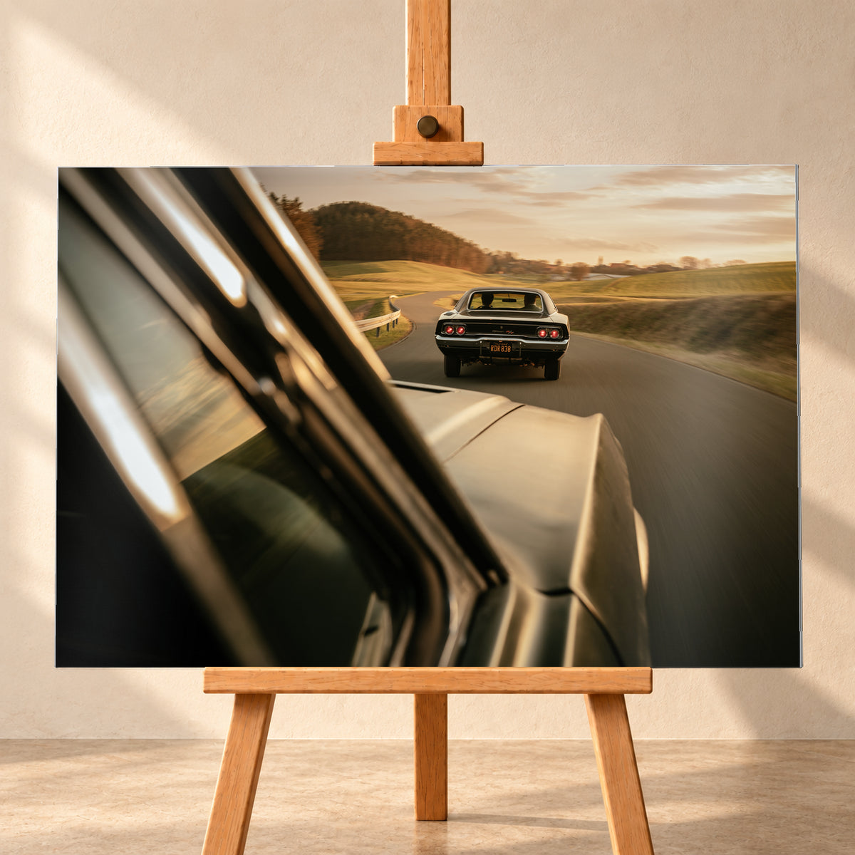 Dunkler Dodge Charger 440 R/T von hinten auf einer kurvigen Landstraße im goldenen Abendlicht, fotografiert aus einem zweiten fahrenden Auto; rote Rückleuchten, Wiesen und Bewegungsunschärfe; Visualisierung als Alu gebürstet-Wandbild, frontal auf einer Holzstaffelei.