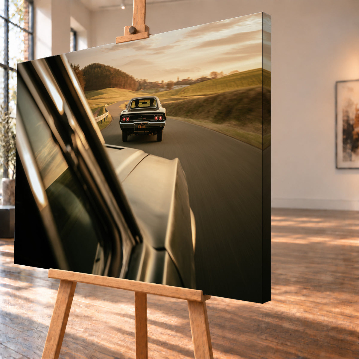 Dunkler Dodge Charger 440 R/T von hinten auf einer kurvigen Landstraße im goldenen Abendlicht, fotografiert aus einem zweiten fahrenden Auto; rote Rückleuchten, Wiesen und Bewegungsunschärfe; Visualisierung als Leinwand-Wandbild, schräg von der Seite auf einer Holzstaffelei.