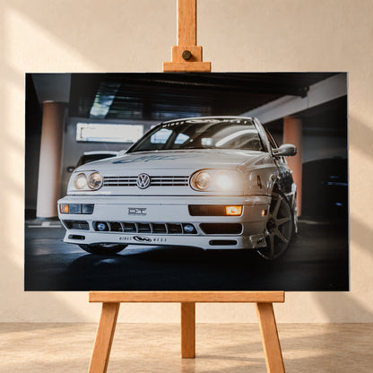 Weißer VW Jetta in niedriger Front-Dreiviertelansicht auf einem dunklen Parkdeck, mit eingeschalteten Scheinwerfern, Dekoren und Startnummer 4. Orangefarbene Säulen, Lichtreflexe und ein unscharfes dunkles Fahrzeug im Hintergrund rahmen die Szene; Visualisierung als Alu gebürstet-Wandbild, frontal auf einer Holzstaffelei.