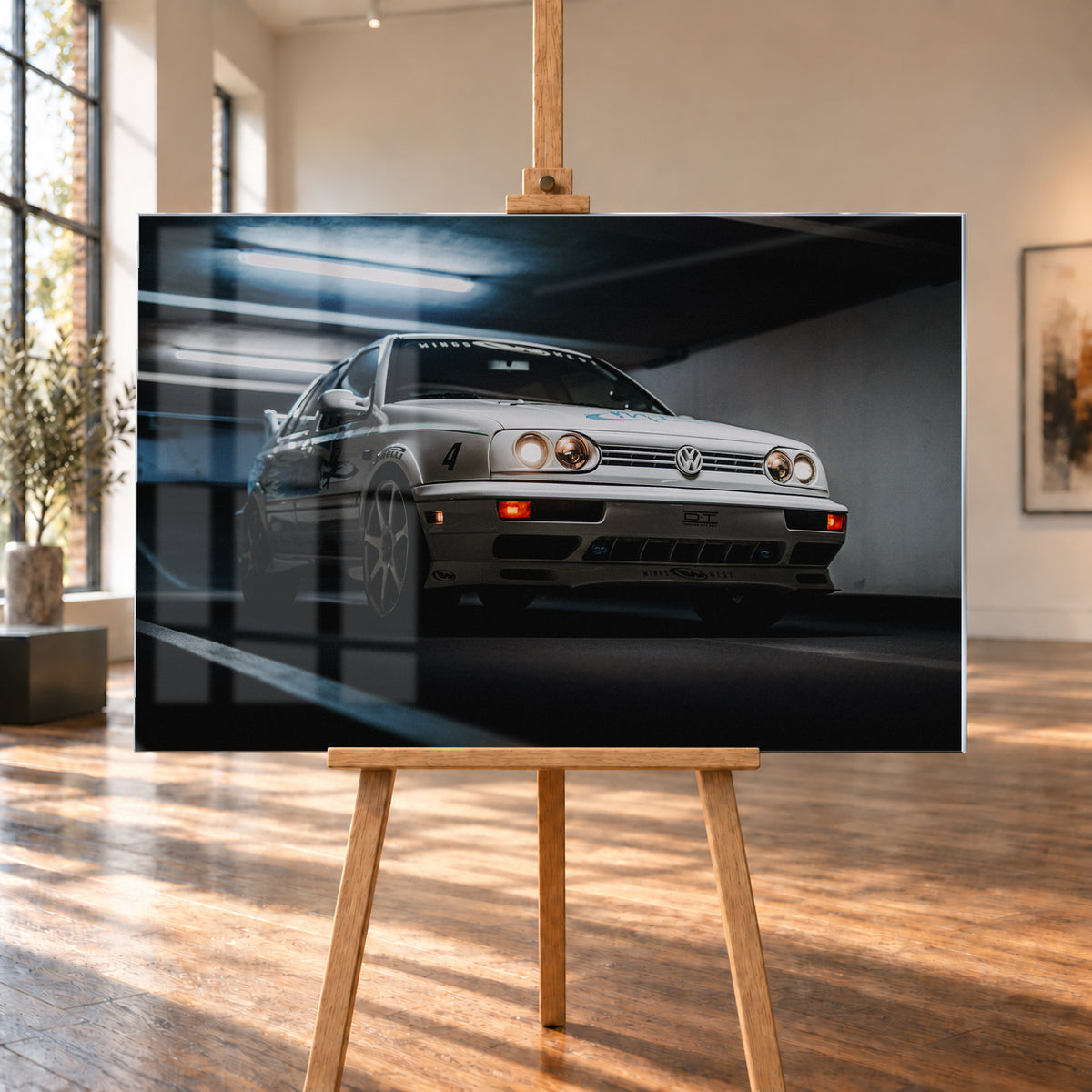 Hellsilberner Volkswagen Jetta mit eingeschalteten Scheinwerfern, grafischen Beklebungen und Nummer 4 in niedriger Front-Dreiviertelansicht auf einer Rampe in einer dunkel und blau beleuchteten Parkgarage; Visualisierung als Acrylglas-Wandbild, auf einer Holzstaffelei in einem hellen Galerieraum.