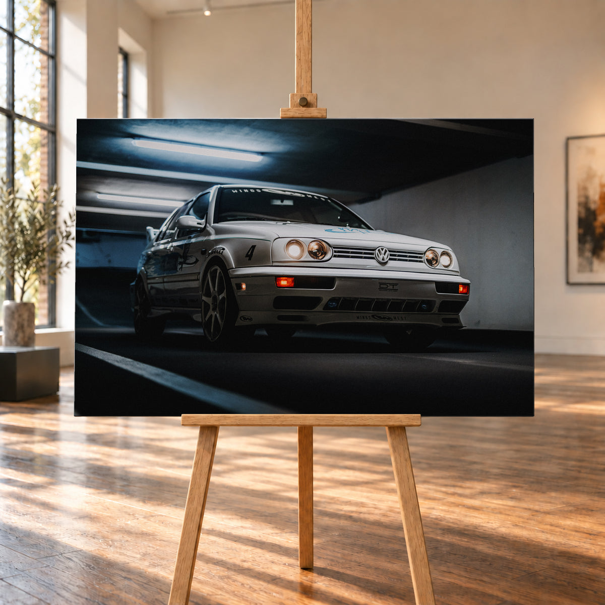 Hellsilberner Volkswagen Jetta mit eingeschalteten Scheinwerfern, grafischen Beklebungen und Nummer 4 in niedriger Front-Dreiviertelansicht auf einer Rampe in einer dunkel und blau beleuchteten Parkgarage; Visualisierung als Leinwand-Wandbild, auf einer Holzstaffelei in einem hellen Galerieraum.