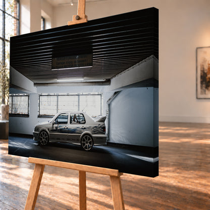 Silberfarbener VW Jetta mit blau-schwarzer Seitengrafik, großen Leichtmetallrädern und hohem Heckflügel im Seitenprofil in einer dunklen Parkgarage; Visualisierung als Leinwand-Wandbild, schräg von der Seite auf einer Holzstaffelei.