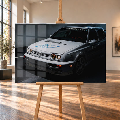 Heller Volkswagen Jetta in frontaler Dreiviertelansicht vor dunklem Hintergrund, mit eingeschalteten runden Frontscheinwerfern, orangefarbenen Leuchten, schwarzen und blauen Grafiken auf der Motorhaube sowie sichtbaren Aufklebern an Scheibe und Karosserie; Visualisierung als Acrylglas-Wandbild, auf einer Holzstaffelei in einem hellen Galerieraum.