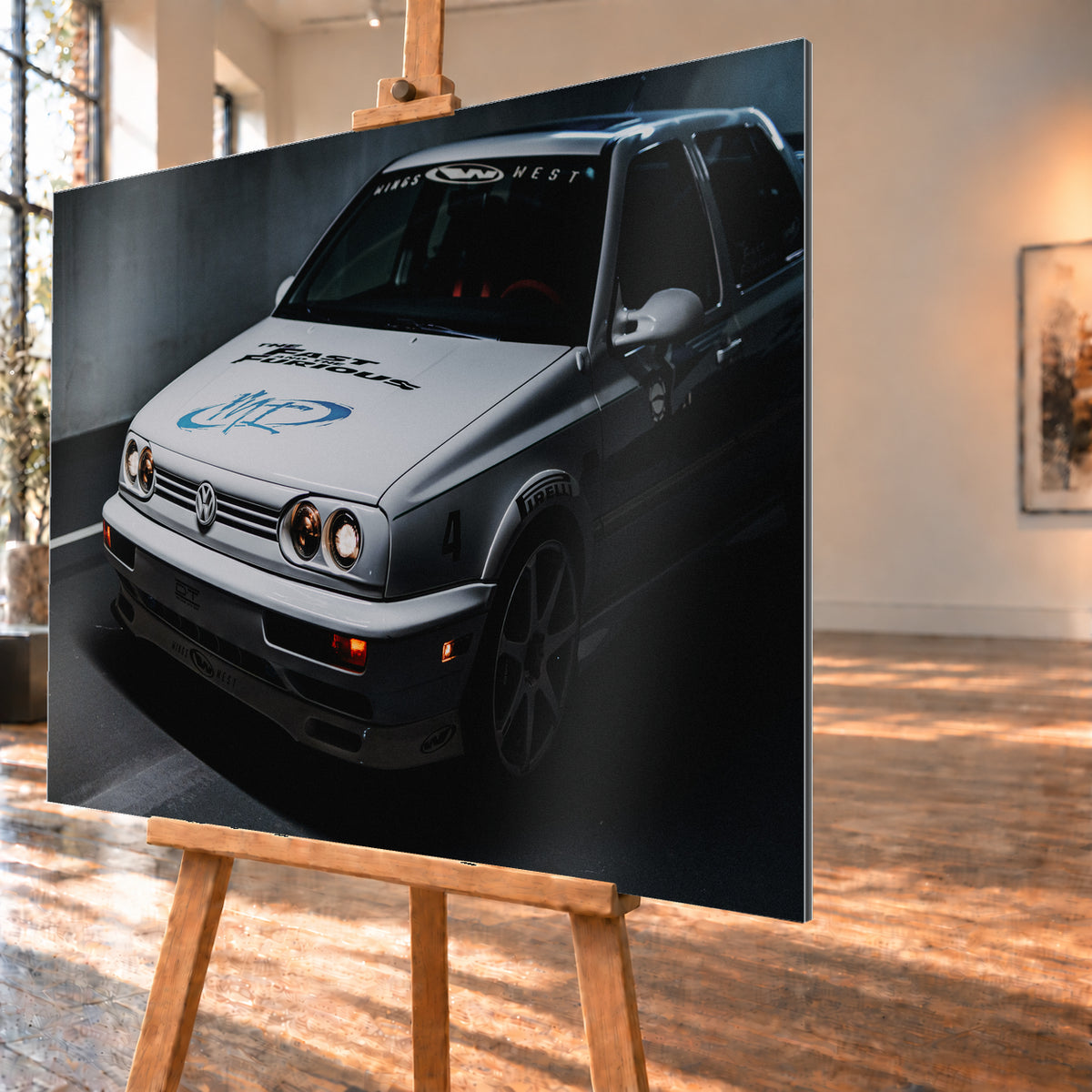 Heller Volkswagen Jetta in frontaler Dreiviertelansicht vor dunklem Hintergrund, mit eingeschalteten runden Frontscheinwerfern, orangefarbenen Leuchten, schwarzen und blauen Grafiken auf der Motorhaube sowie sichtbaren Aufklebern an Scheibe und Karosserie; Visualisierung als Alu gebürstet-Wandbild, schräg von der Seite auf einer Holzstaffelei.