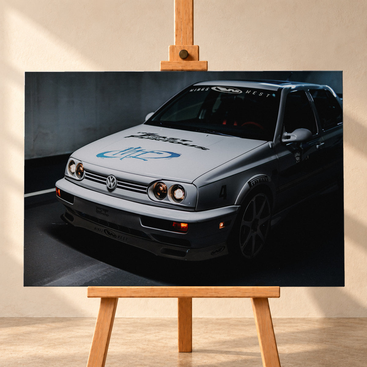 Heller Volkswagen Jetta in frontaler Dreiviertelansicht vor dunklem Hintergrund, mit eingeschalteten runden Frontscheinwerfern, orangefarbenen Leuchten, schwarzen und blauen Grafiken auf der Motorhaube sowie sichtbaren Aufklebern an Scheibe und Karosserie; Visualisierung als Leinwand-Wandbild, frontal auf einer Holzstaffelei.