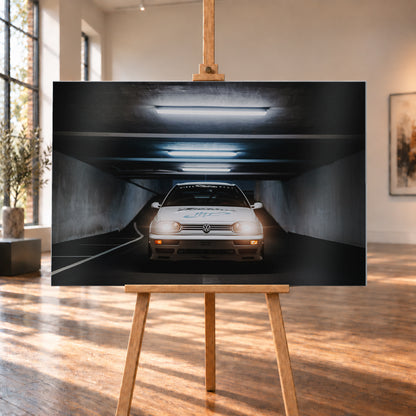 Weißer Volkswagen Jetta in frontaler Ansicht in einer dunklen Betongarage; Scheinwerfer und orangefarbene untere Leuchten sind eingeschaltet, darüber verlaufen helle Deckenröhren; Visualisierung als Alu gebürstet-Wandbild, auf einer Holzstaffelei in einem hellen Galerieraum.