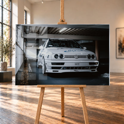 Weißer VW Jetta in tiefer, leicht seitlicher Frontansicht in einer dunklen Parkgarage. Vier runde Scheinwerfer, weiße Räder, Karosseriegrafiken und die Nummer 4 sind sichtbar; links fällt ein heller Lichtkeil auf die Betonwand und die Fahrzeugseite; Visualisierung als Acrylglas-Wandbild, auf einer Holzstaffelei in einem hellen Galerieraum.