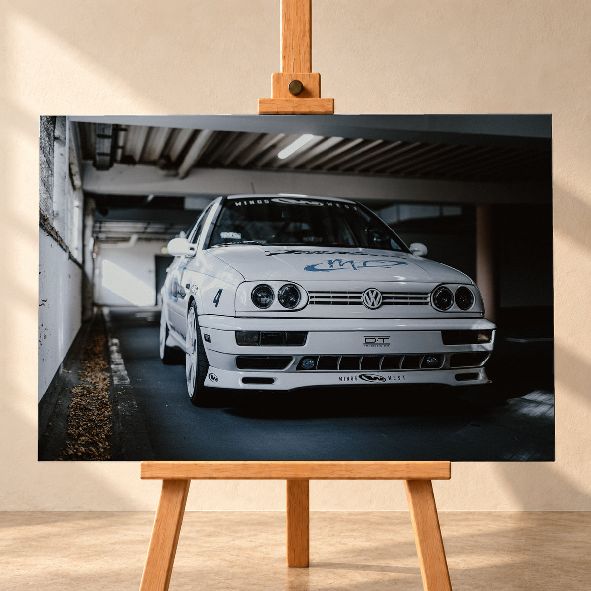 Weißer VW Jetta in tiefer, leicht seitlicher Frontansicht in einer dunklen Parkgarage. Vier runde Scheinwerfer, weiße Räder, Karosseriegrafiken und die Nummer 4 sind sichtbar; links fällt ein heller Lichtkeil auf die Betonwand und die Fahrzeugseite; Visualisierung als Leinwand-Wandbild, frontal auf einer Holzstaffelei.