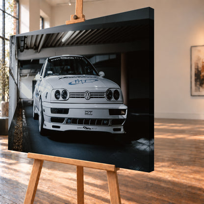 Weißer VW Jetta in tiefer, leicht seitlicher Frontansicht in einer dunklen Parkgarage. Vier runde Scheinwerfer, weiße Räder, Karosseriegrafiken und die Nummer 4 sind sichtbar; links fällt ein heller Lichtkeil auf die Betonwand und die Fahrzeugseite; Visualisierung als Leinwand-Wandbild, schräg von der Seite auf einer Holzstaffelei.