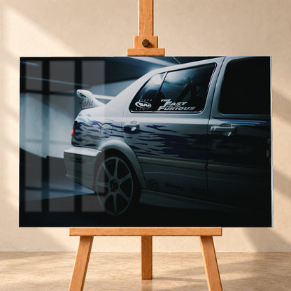 Nahaufnahme der hinteren Seitenpartie eines hellen VW Jetta mit blau-violetter Flammengrafik, großem Rad und Heckflügel. Im dunklen Seitenfenster steht „The Fast and the Furious“; kühles Licht fällt auf Wand und Boden; Visualisierung als Acrylglas-Wandbild, frontal auf einer Holzstaffelei.