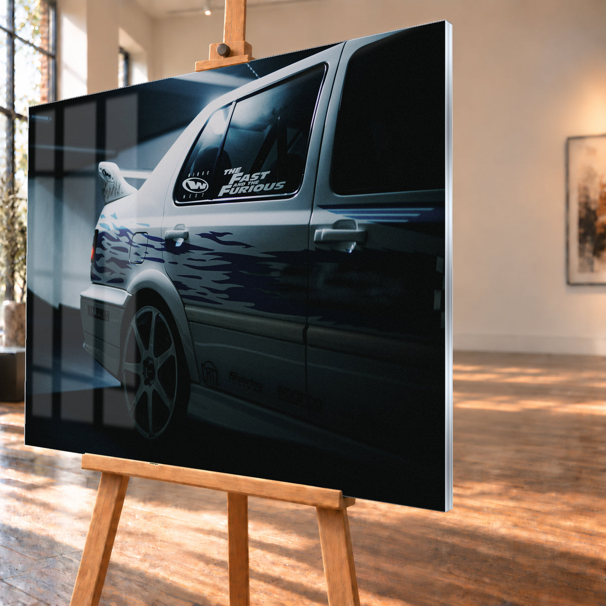 Nahaufnahme der hinteren Seitenpartie eines hellen VW Jetta mit blau-violetter Flammengrafik, großem Rad und Heckflügel. Im dunklen Seitenfenster steht „The Fast and the Furious“; kühles Licht fällt auf Wand und Boden; Visualisierung als Acrylglas-Wandbild, schräg von der Seite auf einer Holzstaffelei.
