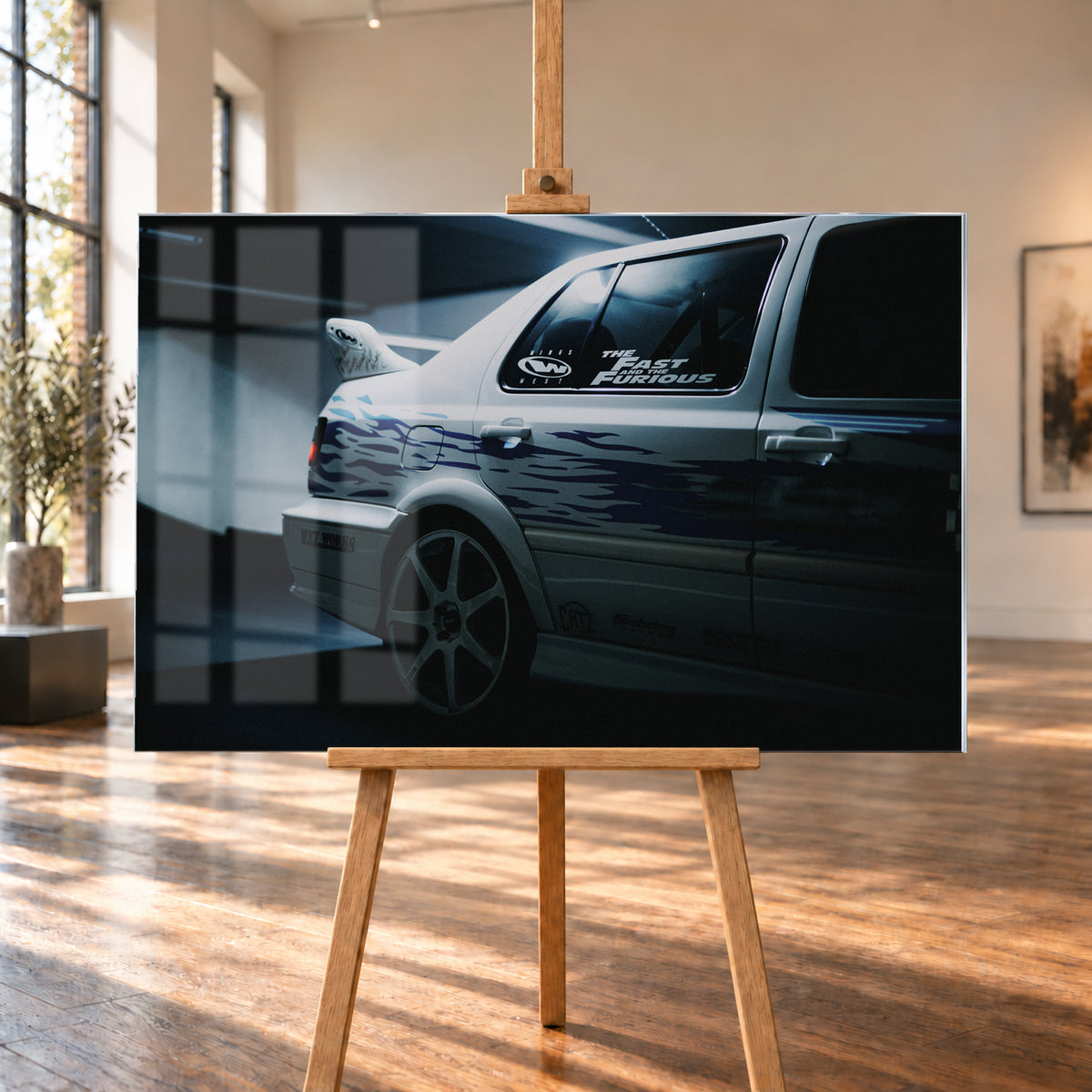 Nahaufnahme der hinteren Seitenpartie eines hellen VW Jetta mit blau-violetter Flammengrafik, großem Rad und Heckflügel. Im dunklen Seitenfenster steht „The Fast and the Furious“; kühles Licht fällt auf Wand und Boden; Visualisierung als Acrylglas-Wandbild, auf einer Holzstaffelei in einem hellen Galerieraum.