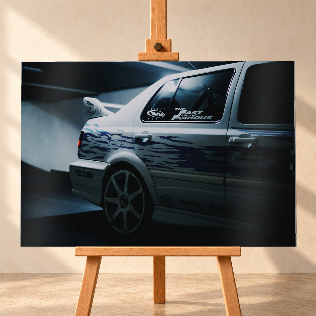 Nahaufnahme der hinteren Seitenpartie eines hellen VW Jetta mit blau-violetter Flammengrafik, großem Rad und Heckflügel. Im dunklen Seitenfenster steht „The Fast and the Furious“; kühles Licht fällt auf Wand und Boden; Visualisierung als Alu gebürstet-Wandbild, frontal auf einer Holzstaffelei.