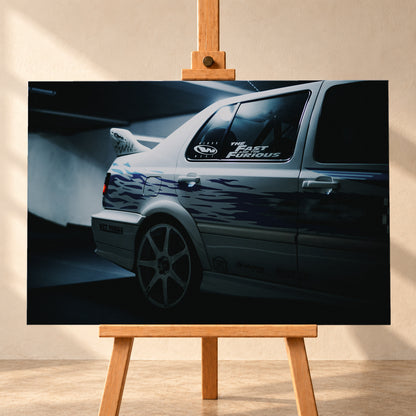 Nahaufnahme der hinteren Seitenpartie eines hellen VW Jetta mit blau-violetter Flammengrafik, großem Rad und Heckflügel. Im dunklen Seitenfenster steht „The Fast and the Furious“; kühles Licht fällt auf Wand und Boden; Visualisierung als Leinwand-Wandbild, frontal auf einer Holzstaffelei.