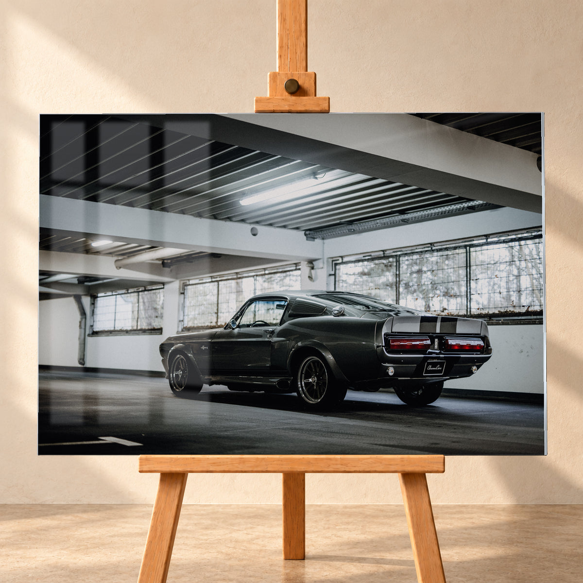 Dunkelgraue Eleanor mit hellen Doppelstreifen in tiefer Heck-Dreiviertelansicht auf einer leeren Parkebene mit weißen Trägern, großen Fenstern und kühlem Deckenlicht; Visualisierung als Acrylglas-Wandbild, frontal auf einer Holzstaffelei.